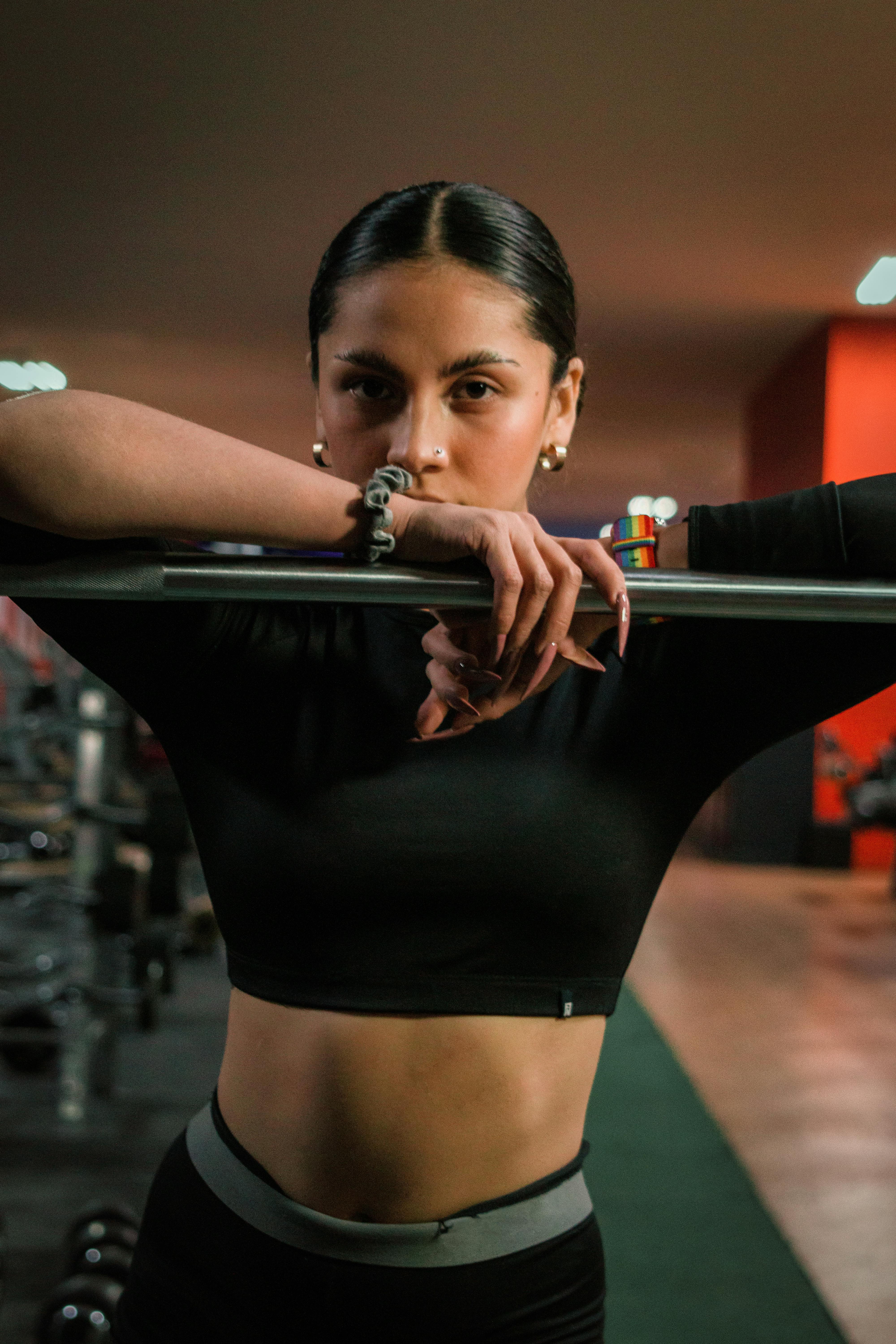 Home Portrait of a confident female athlete in gymwear leaning on a barbell in a gym setting.