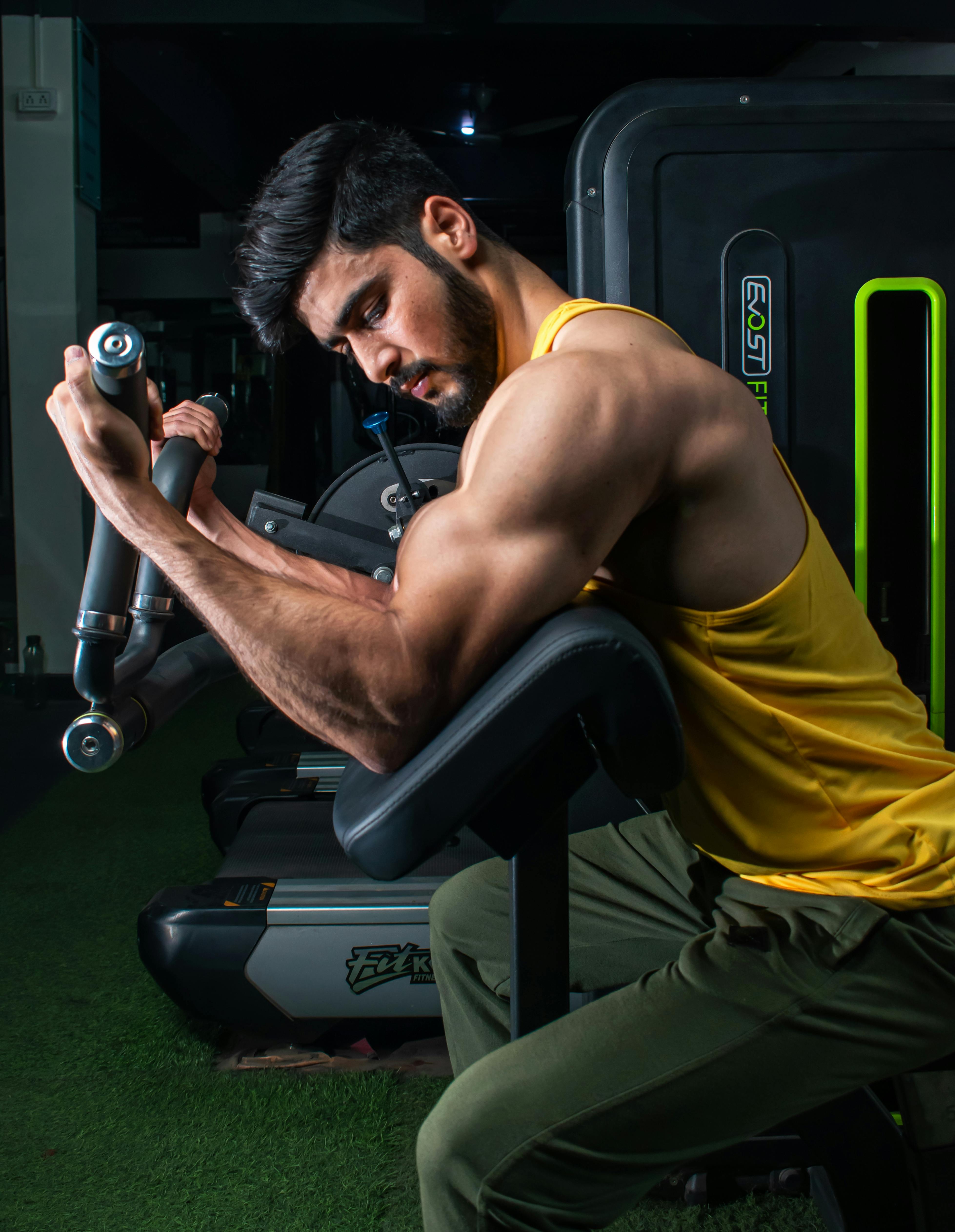 Home Muscular man in a gym performing bicep curls on a machine, showcasing strength and dedication.