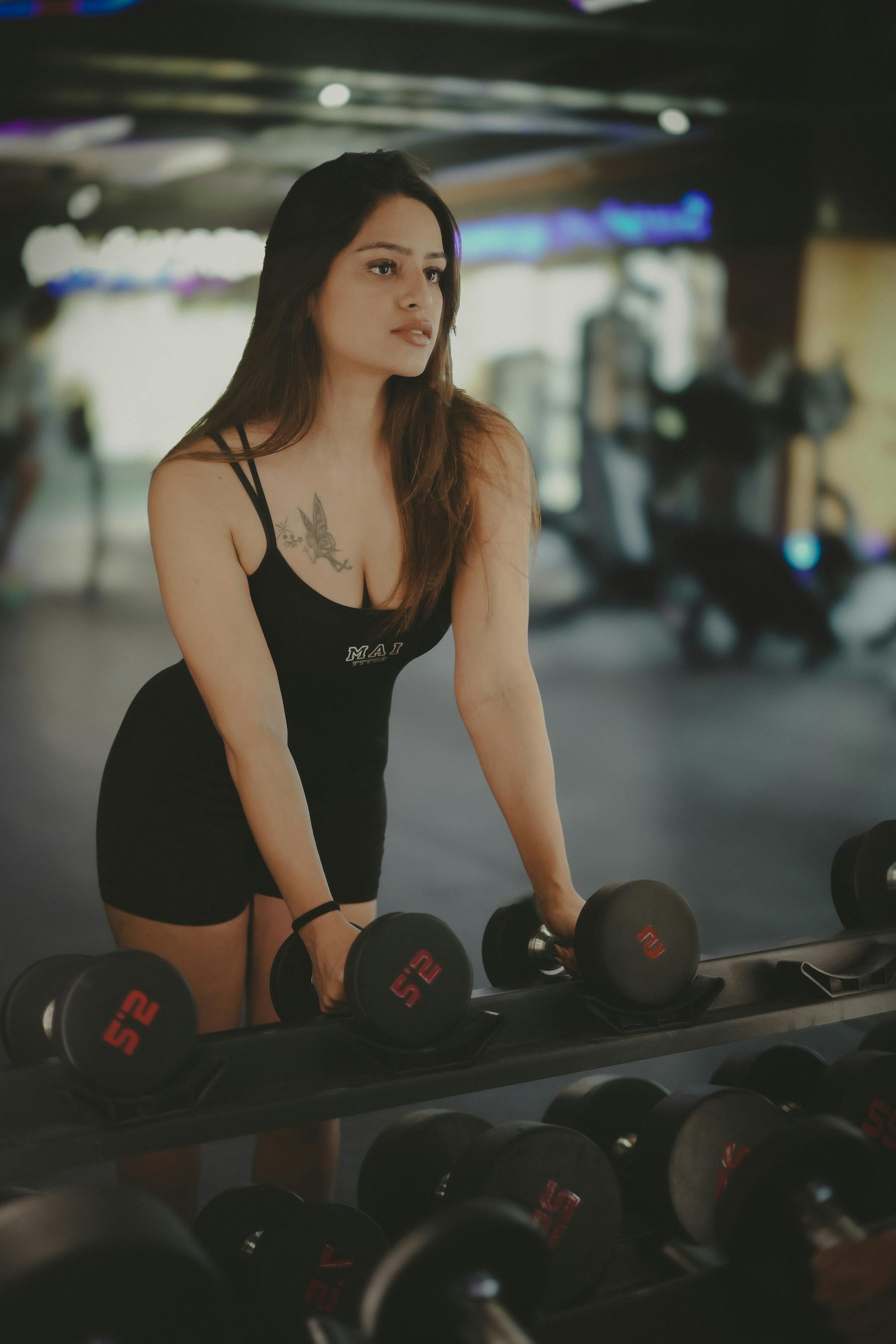 Home Athletic woman in black sportswear working out with dumbbells at the gym.